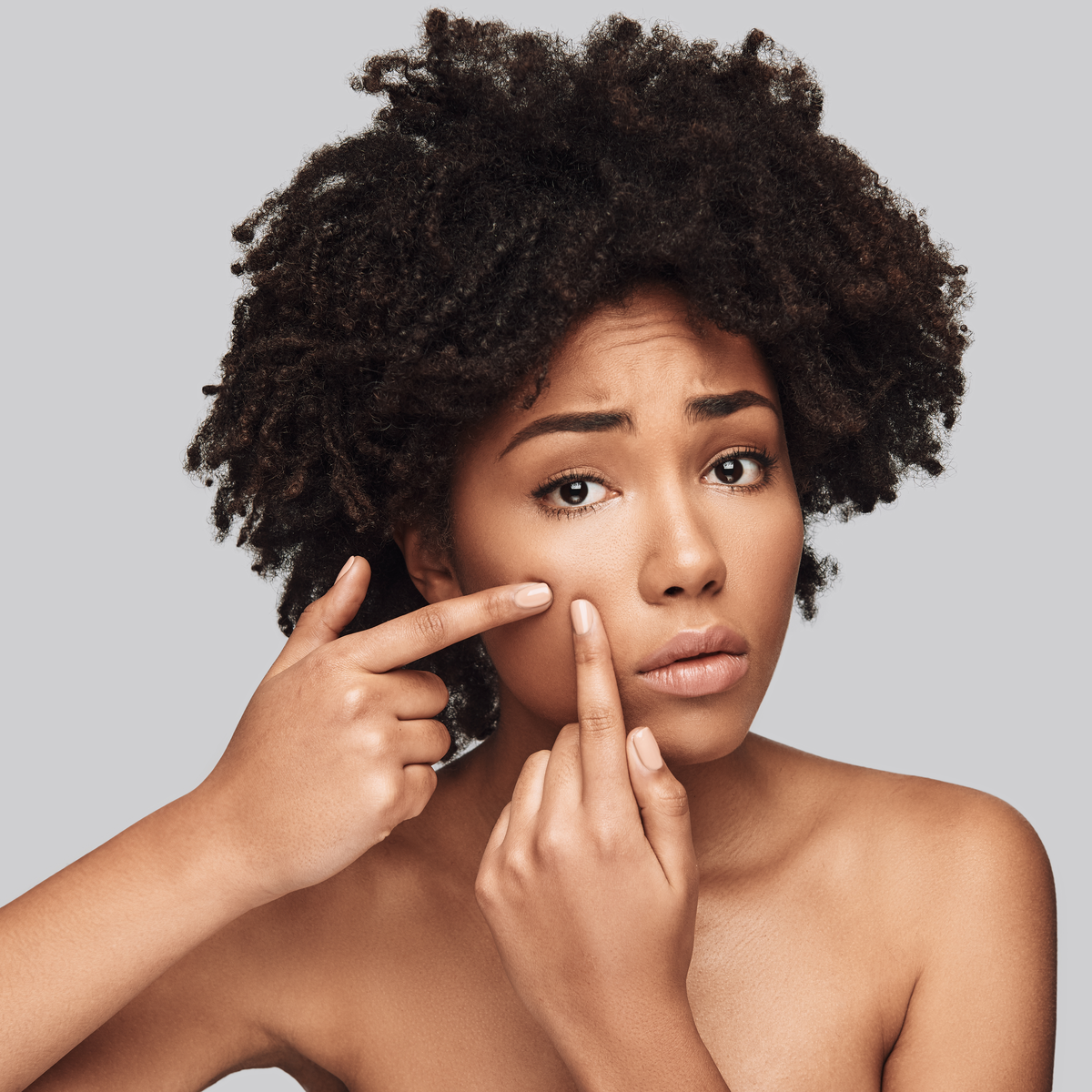 Black woman, looking worried, popping a pimple in her cheek